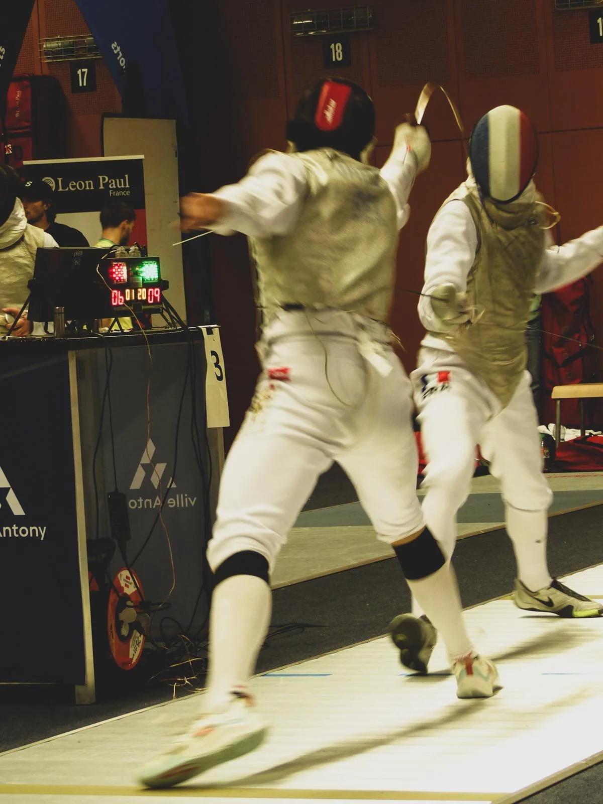 Two foil fencers in a competition bout beside the scoring apparatus.