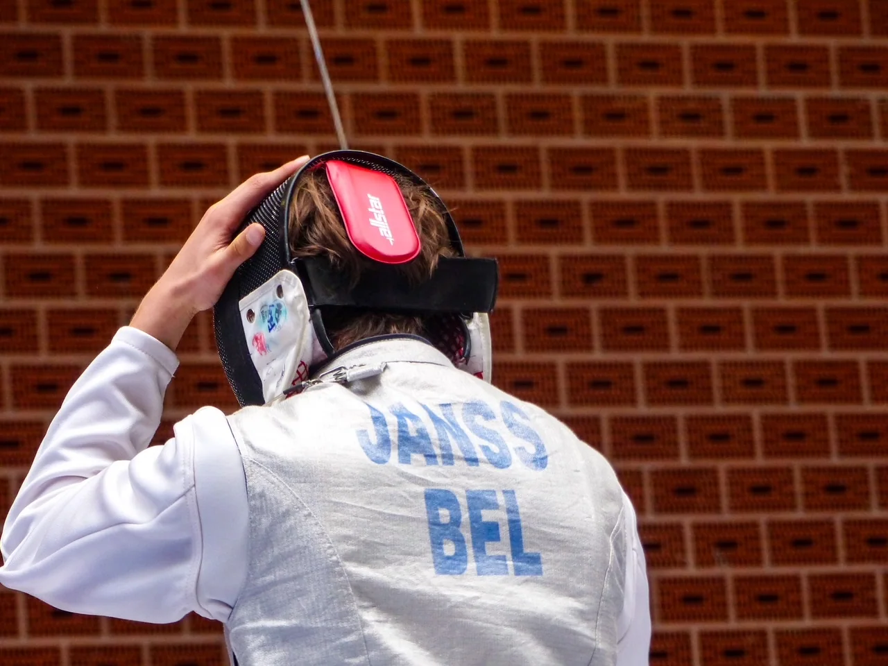 The back of Luca’s fencing jacket, marked JANSS BEL, as he lifts his mask.