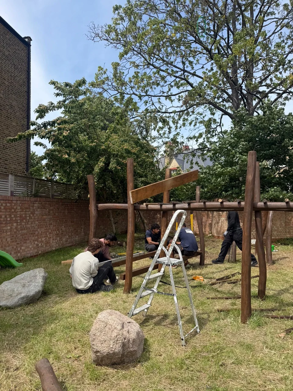 Volunteers assembling a timber frame in an outdoor play space.
