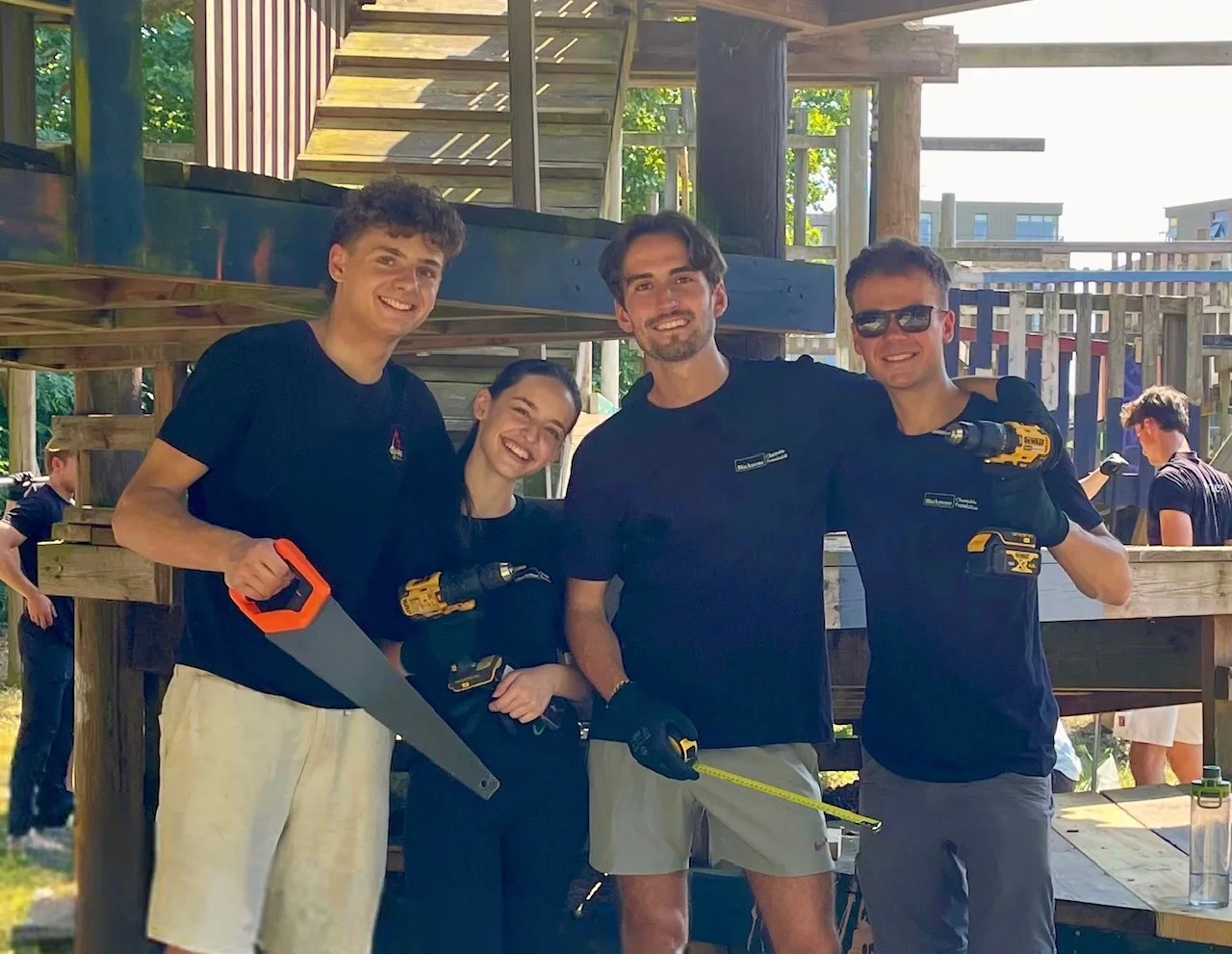 Four volunteers with tools in front of an outdoor play structure.