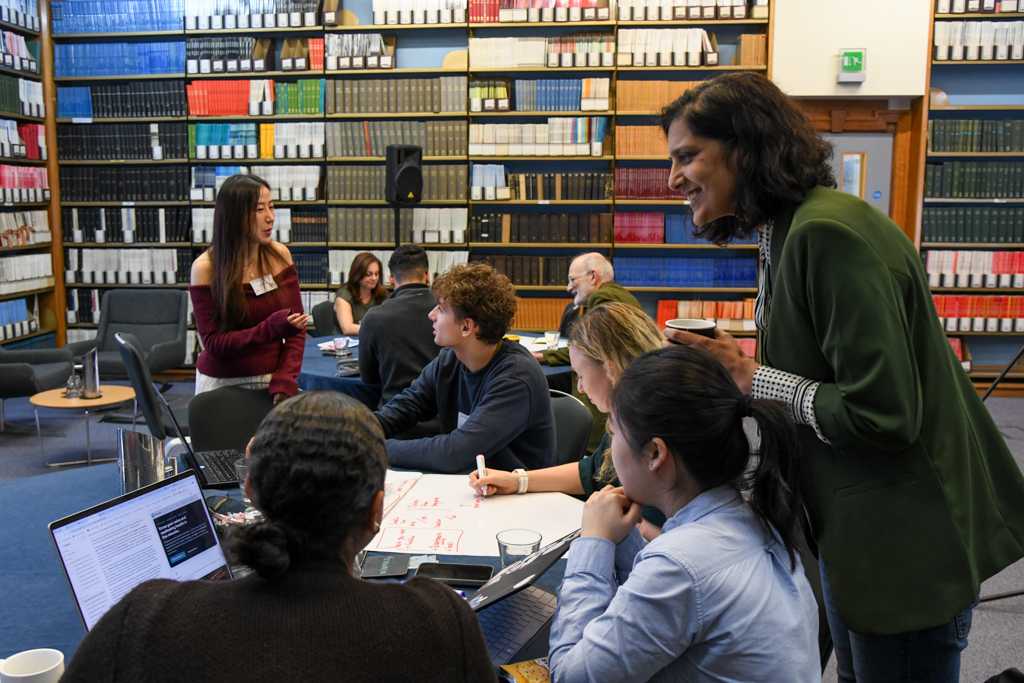 VoiceWell workshop participants discussing ideas around a table with laptops and handwritten notes in a library.